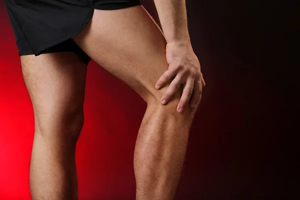 Młody człowiek z bólem kolana, na czerwonym tle — Zdjęcie stockowe
