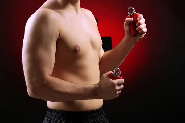 Handsome young muscular sportsman with expanders, on dark background — Stock Photo, Image