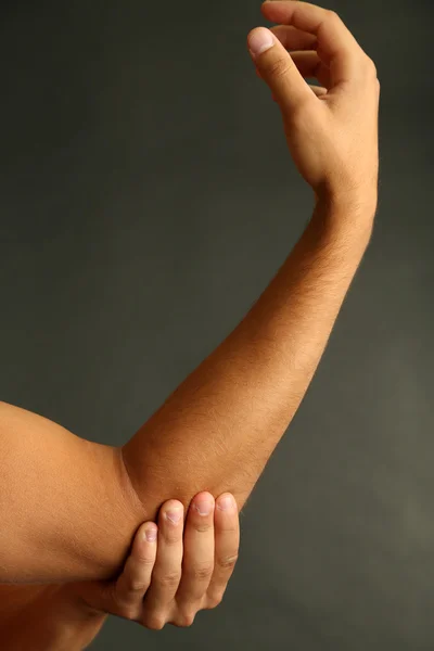 Junger Mann mit Schmerzen in der Hand auf grauem Hintergrund — Stockfoto