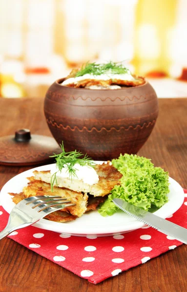 Potato pancakes in pot, on wooden table, on bright background — Stock Photo, Image