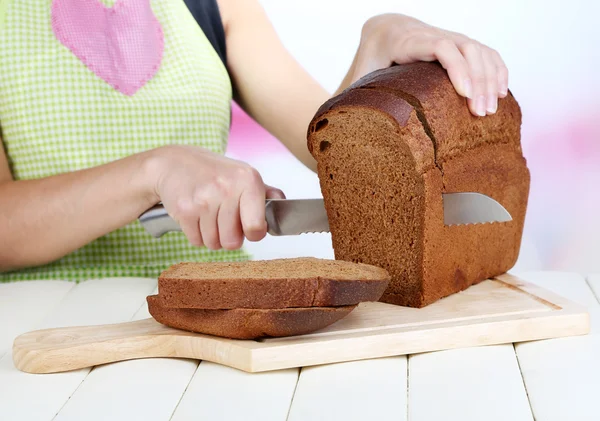 Cutting bread on wooden board on wooden table on bright background — Stock Photo, Image