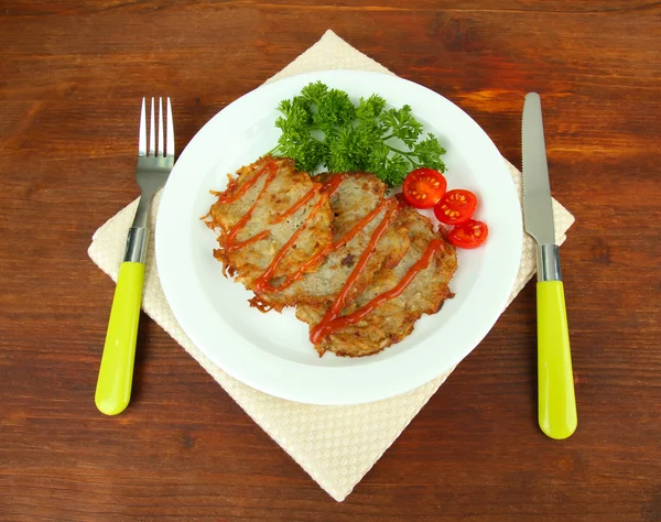 Картофельные блинчики на тарелке, на деревянном фоне — стоковое фото