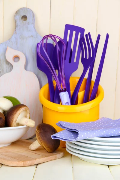 Plastic kitchen utensils in cup on wooden table — Stock Photo, Image