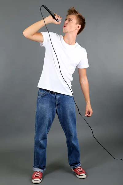 Pohledný mladý muž zpívá na šedém pozadí — Stock fotografie