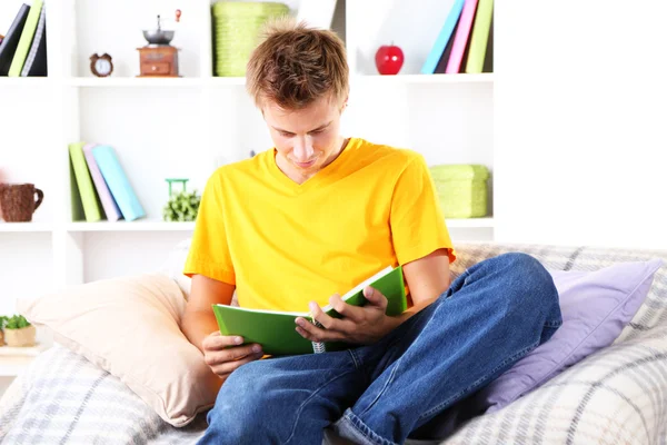 Hombre joven relajándose en el sofá con libro — Foto de Stock