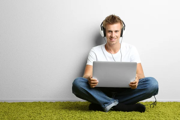 Young man relaxing on carpet and listening to music, on gray wall background — Stock Photo, Image