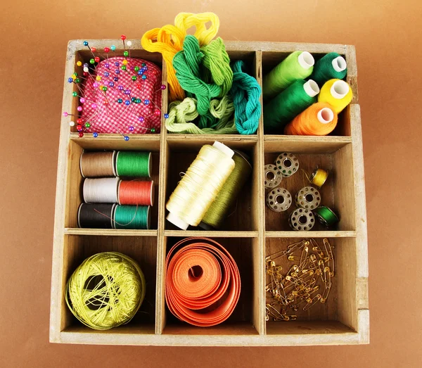 Thread and sewing tools in box on brown background — Stock Photo, Image