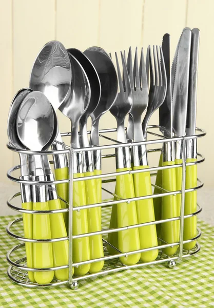 Cuchillos, tenedores y cucharas en soporte de metal sobre mesa sobre fondo brillante —  Fotos de Stock