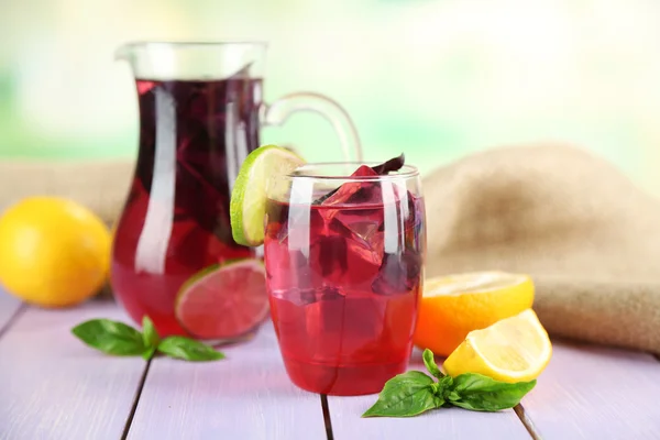 Red basil lemonade in jug and glass, on wooden table, on bright background — Stock Photo, Image