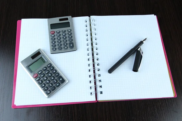 Caderno com caneta e calculadoras sobre fundo de madeira — Fotografia de Stock