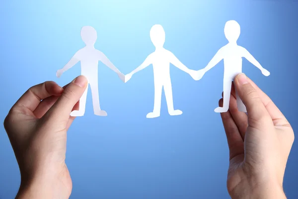 Paper people in hands on blue background — Stock Photo, Image