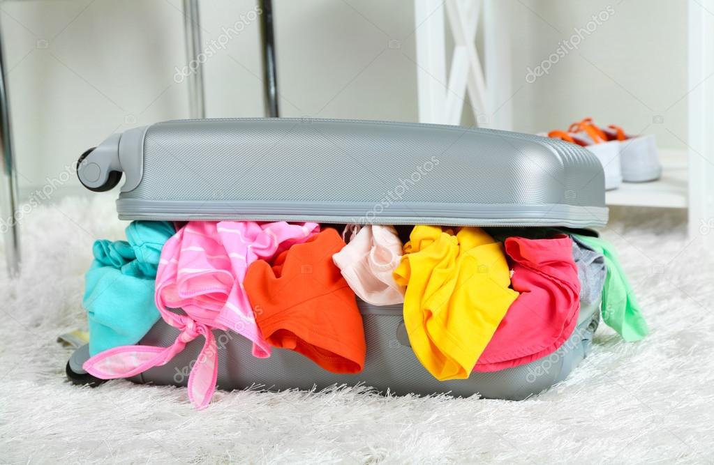 Suitcase with clothes on carpet on room background