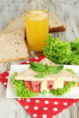 Lezzetli sandviç salam sosis ve parlak zemin üzerine ahşap masa üzerinde renkli peçete üzerinde sebze ve meyve suyu ile kompozisyon