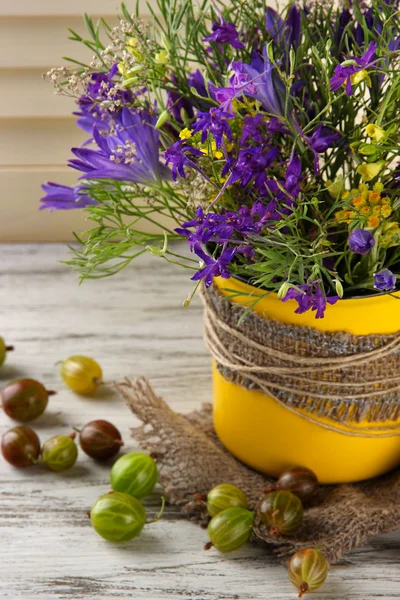 Vacker bukett av blommor i kopp och bär på träbord — Stockfoto