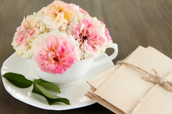 Roses in cup on napkins on wooden background — Stock Photo, Image