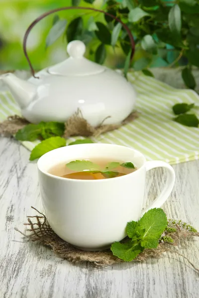 Tetera y taza de té de hierbas con menta fresca en la mesa de madera — Foto de Stock