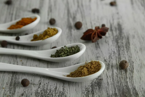 Assortimento di spezie in cucchiai bianchi, su fondo di legno — Foto Stock