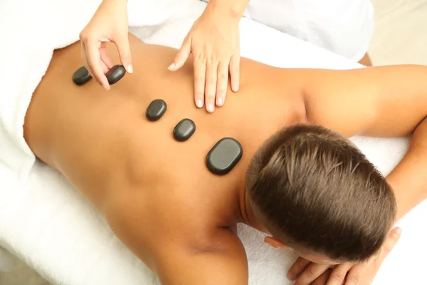 Joven hombre teniendo masaje de piedra en el salón de spa — Foto de Stock