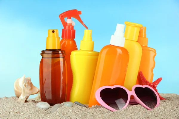 Bottles with suntan cream and sunglasses, on blue background — Stock Photo, Image