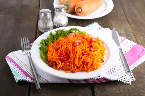 Carrot salad on plate on napkin on wooden table — Stock Photo, Image