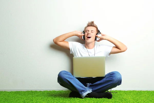 Jonge man ontspannen op tapijt en luisteren naar muziek, op grijze muur achtergrond — Stockfoto