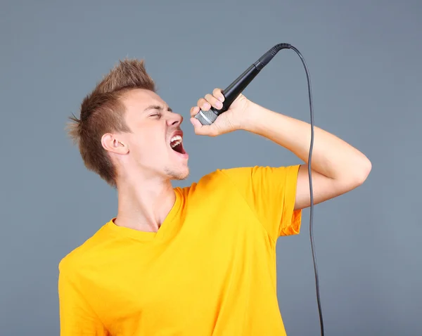 Handsome young man sings on grey background — Stock Photo, Image