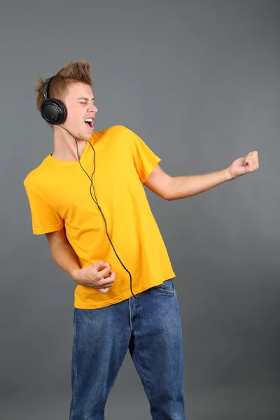 Bel giovanotto che ascolta musica su sfondo grigio — Foto Stock