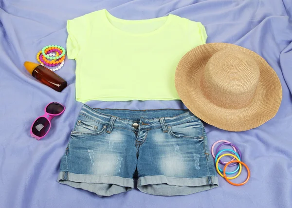 Top, shorts and beach items on bright purple background — Stock Photo, Image