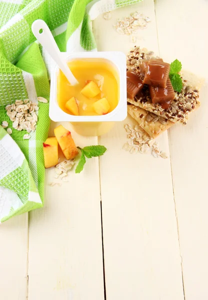 Iogurte saboroso com pedaços de frutas frescas, biscoitos e flocos, na cor de fundo de madeira — Fotografia de Stock