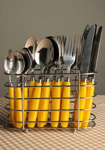 Knives, forks and spoons in metal stand on tablecloth on grey background — Stock Photo, Image