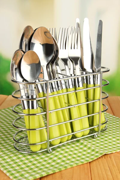 Knives, forks and spoons in metal stand on table on bright background — Stock Photo, Image