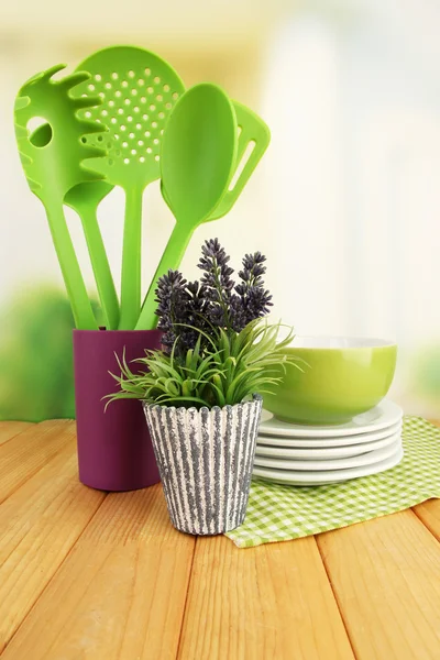 Utensílios de cozinha de plástico em stand com pratos limpos na mesa sobre fundo brilhante — Fotografia de Stock