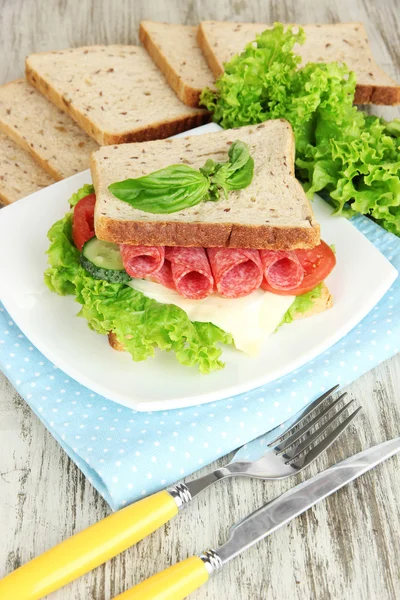 Composizione con succo di frutta e gustoso sandwich con salsiccia di salame e verdure su tovagliolo di colore, su sfondo tavolo di legno — Foto Stock