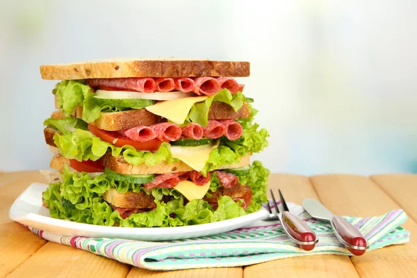Huge sandwich on wooden table, on light background — Stock Photo, Image