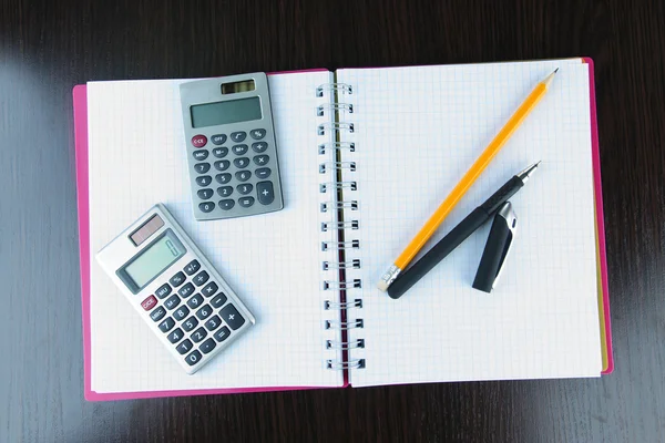 Cuaderno con pluma, lápiz y calculadoras sobre fondo de madera — Foto de Stock