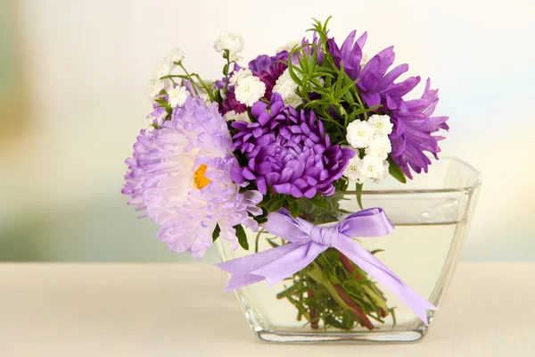 Красивый букет ярких цветов в стеклянной вазе, на деревянном столе, на ярком фоне — стоковое фото