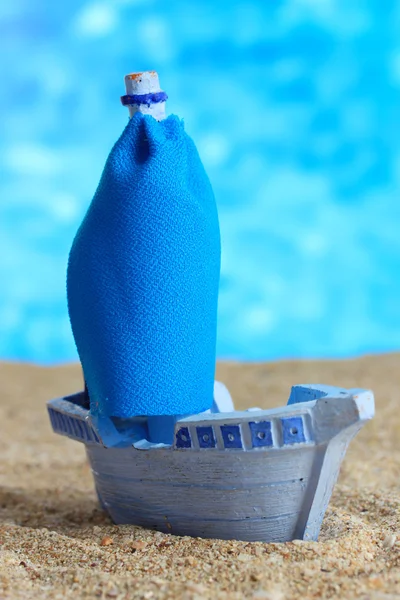 Синій іграшковий корабель на піску, на синьому фоні — стокове фото