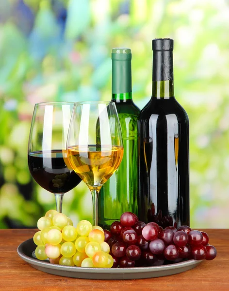 Wine bottles and glasses of wine on tray, on bright background — Stock Photo, Image