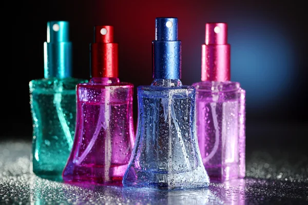 Vrouwen parfum in mooie flessen op donkere achtergrond met kleur licht — Stockfoto