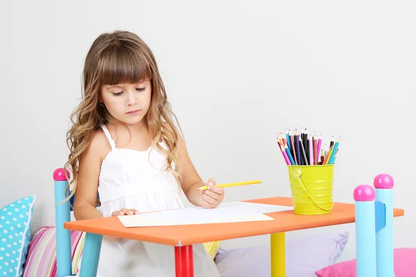 Küçük kız oturma odasındaki masada gri duvar zemin üzerine çizer — Stok fotoğraf