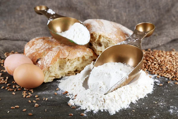 The wholemeal flour in scoops on wooden table on sackcloth background — Stock Photo, Image