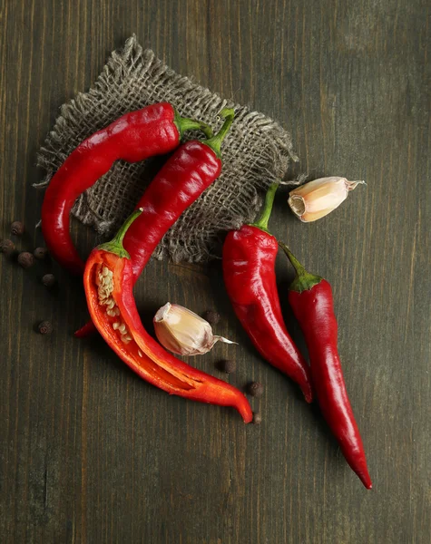 Red hot chili peppers and garlic, on sackcloth, on wooden background — Stock Photo, Image