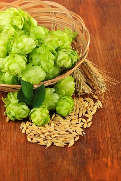 Verse groene hop in rieten mand en gerst, op houten achtergrond — Stockfoto