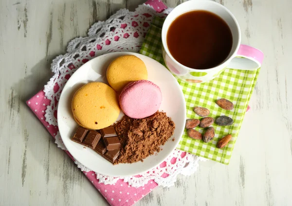 Cocoa in cup with sweets and cocoa powder on plate on wooden table — Stock Photo, Image