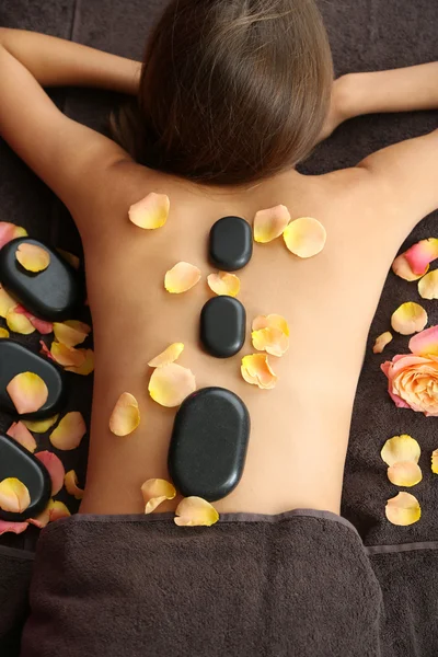 Mooie jonge vrouw met stenen massage in de spa salon over kleur achtergrond — Stockfoto