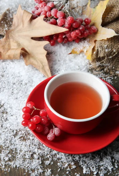 Натюрморт с вибурнумом чай в чашке, ягоды и снег, на деревянном фоне — стоковое фото