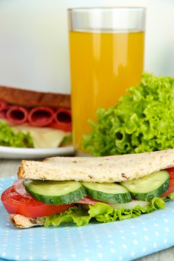 Lezzetli sandviç salam sosis ve parlak zemin üzerine ahşap masa üzerinde renkli peçete üzerinde sebze ve meyve suyu ile kompozisyon