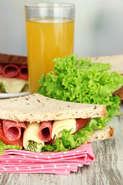 Composition with fruit juice and tasty sandwich with salami sausage and vegetables on color napkin, on wooden table, on bright background — Stock Photo, Image