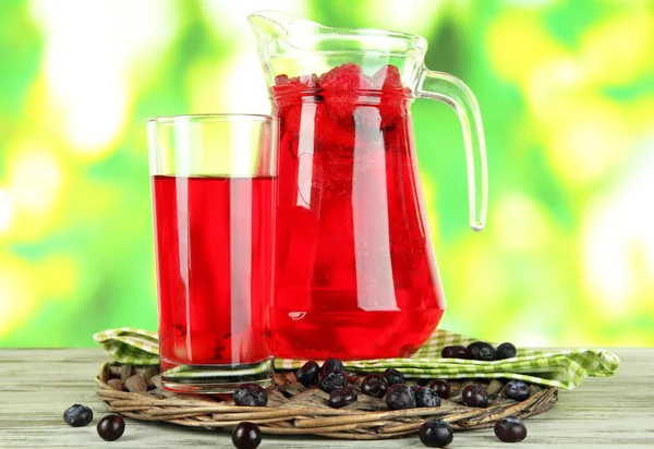 Pitcher and glass of compote on napkin on wooden table on nature background — Stock Photo, Image