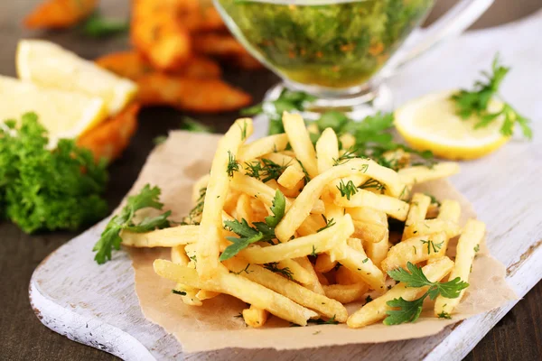 French fries on tracing paper on board on wooden table — Stock Photo, Image